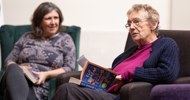 Two women sit reading books from the Libraries2U service