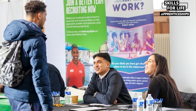 A young person stands in front of two council officers on a stall at an Apprenticeship Fair