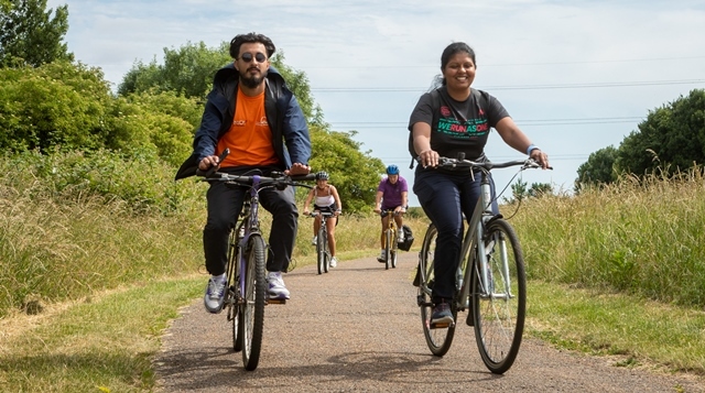 A man and woman ride bikes surrounded by grass and trees on the Tour de Waltham Forest 2022