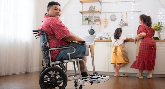 A man with a prosthetic leg sits in a wheelchair while a young girl and older woman work at a sink