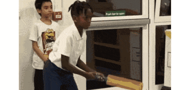 A child in school uniform swings a cricket bat at a ball while another child fields
