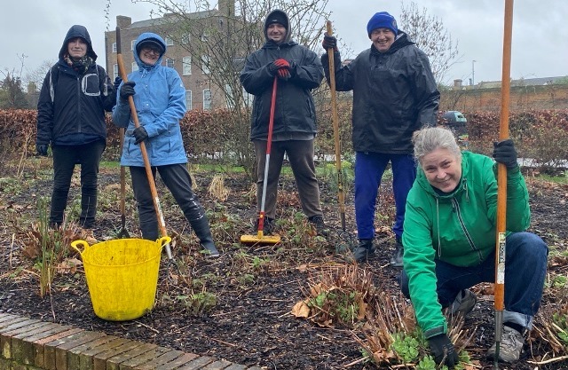 A group of people work in flowers beds in Lloyd Park with William Morris Gallery behind