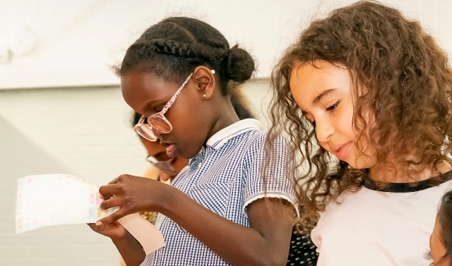 A school girl reads a letter while another child looks down beside her