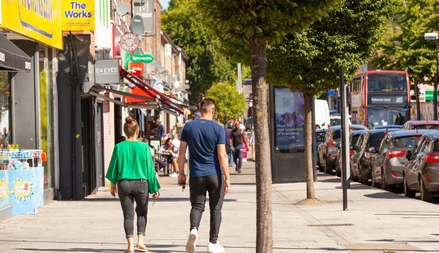 Two people stroll down a shopping street in the sunshine