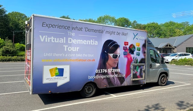 A parked van with The Virtual Dementia Tour logo on the side, showing a woman wearing a VR headset.