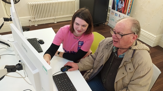 A woman in a Digital Champion sweatshirt shows a man something on a computer screen