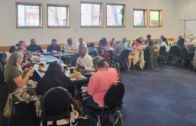 A large group of people sit at tables talking at the Togetherness Cafe