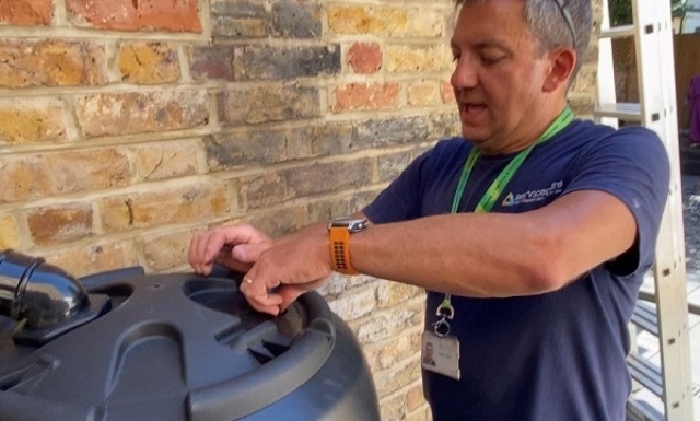 A council officer installs a water butt against a brick wall