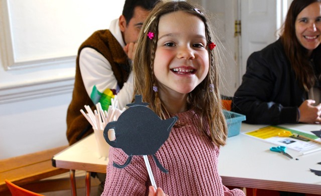 A child with brains in her hair holds up a cardboard tea pot on a stick