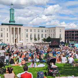 Fellowship Square, people sitting on the grass lawn watching a big screen.