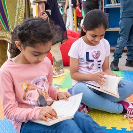 Two children seated on mats, reading. 