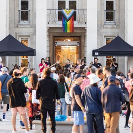 Group of people watching a band in front of a Pride flag.