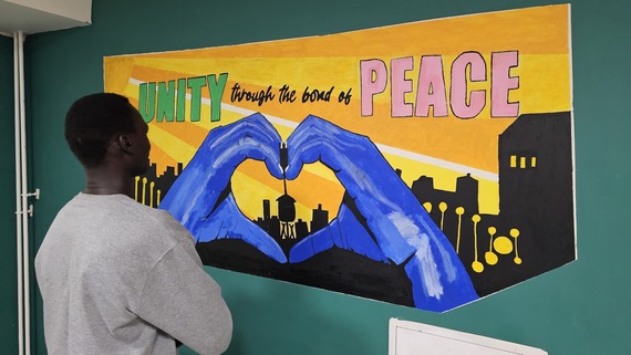 a photo of a man in front of a sign saying: Unity Through the Bond of Peace