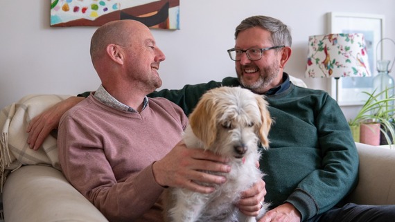 A photo of some men sitting on a couch with a dog