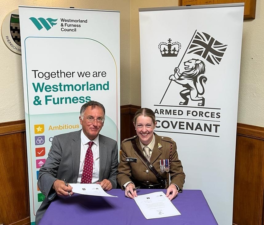Councillor Jonathan Brook and Major Jennifer Henry sat at a table signing the national Armed Forces Covenant.