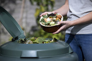 A person adding a bowl of food waste to their compost bin