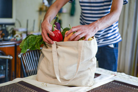 A man unpacking groceries at kitchen island. He is removing fruits and vegetables from reusable bags.