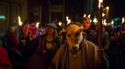 A line of people carrying lit torches at night as part of a parade, one of them wearing an animal mask