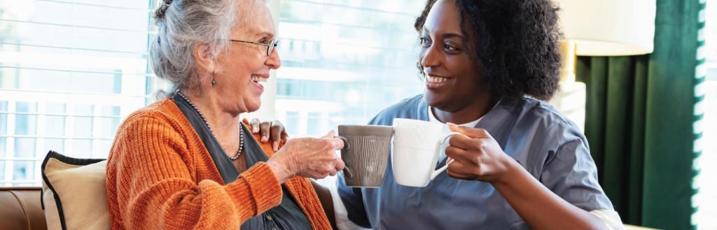 Two women sitting side by side holding mugs and chatting