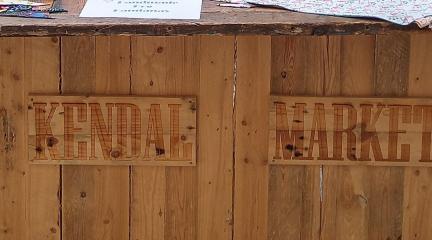 A wooden stall with the words Kendal Market on the side