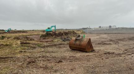 A digger in front of a cleared section of land