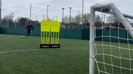 A man on an astro turf pitch kicking a football towards a net