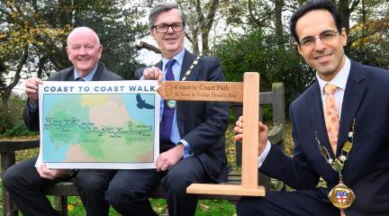 Chairs of Westmorland and Furness, North Yorkshire and Cumberland Councils holding mini Coast to Coast wooden sign and map