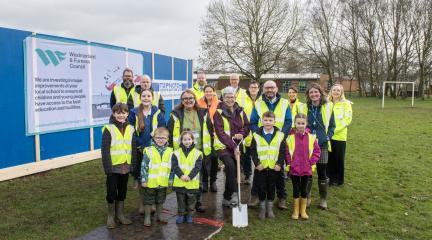 Stakeholders and children at Besconside School with a spade in the ground
