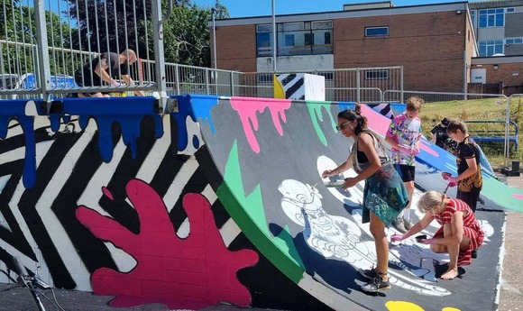 Adults and children working together to paint skate park ramp.