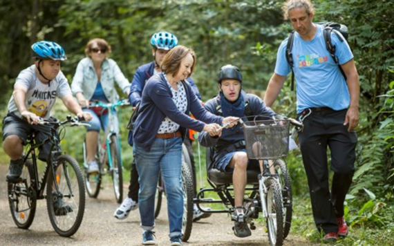 Three people on two wheeled bikes and one on a three wheeled bike being supported by two staff members from My Journey