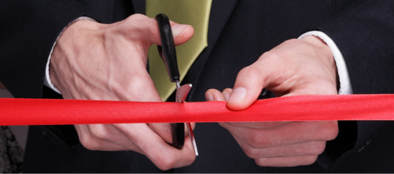 stock photo showing close-up of a man's hands using a pair of scissors to cut a ribbon