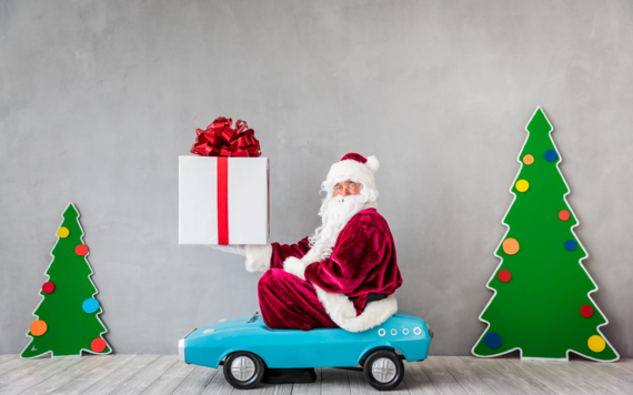 Santa sitting on a small blue car holding a present