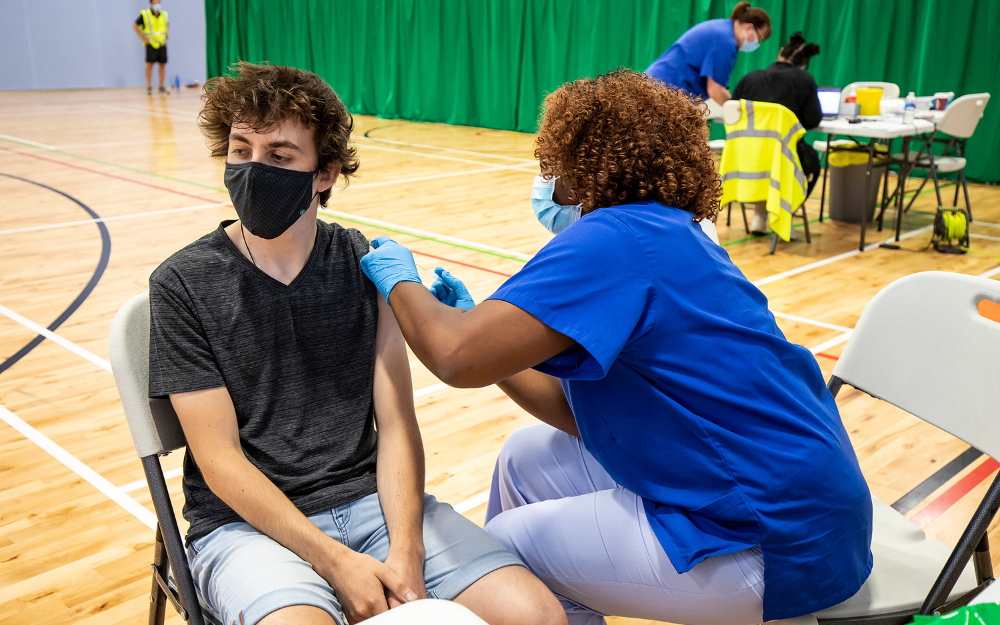 A young man receives his Covid-19 vaccine from a nurse in a leisure centre