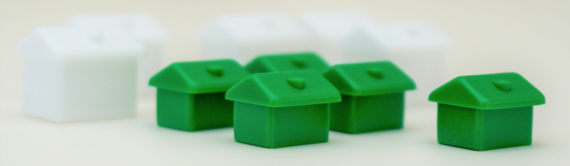 A close-up photograph of some green plastic houses from a popular board game