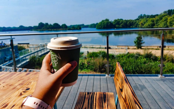 Person holding a coffee cup in front of the view from Dinton Activity Centre