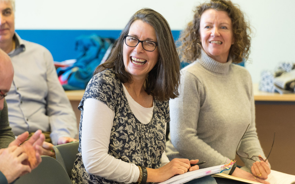 A woman holding an annotated book smiles as she takes part in a class at the Rebel Business School