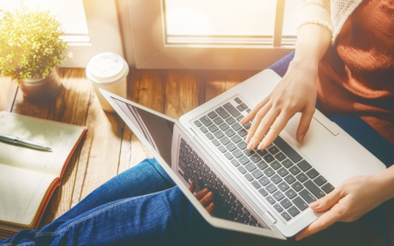 Soft focus image of a woman from the neck down relaxing on a wooden floor whilst looking at a laptop