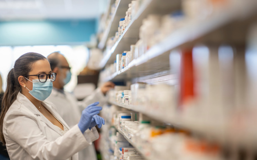 A pharmacist working in a pharmacy, looking at medication on shelving