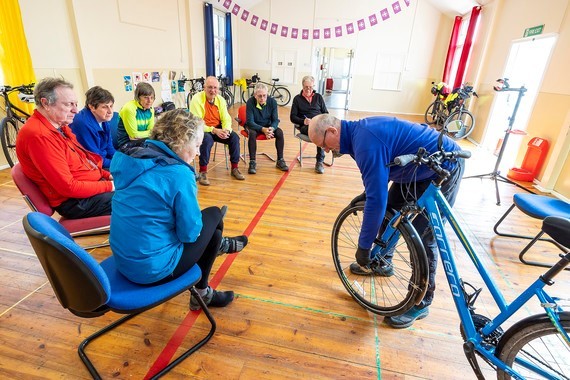 Image showing a group of cyclists attending a MyJourney basic bike maintenance workshop and being shown how to remove their bike wheels