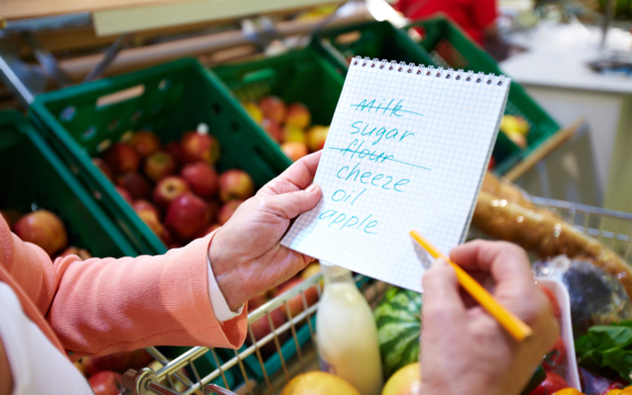 Fruit and vegetables in a supermarket with a close up of a person holding a shopping list and pen