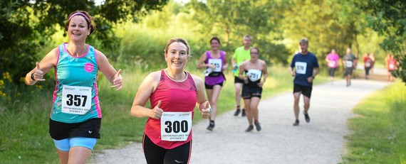 photograph of two smiling women running towards the camera with other runners approaching behind them