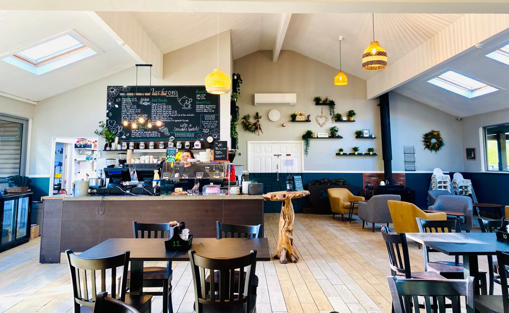 inside Jackson's Café at California Country Park, showing a bright open interior with a counter display carrying food and young woman at the till.