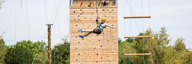 photo of a happy young boy hanging from a climbing rope while wearing a safety helmet and harness