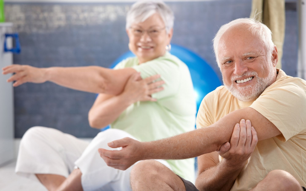 An older man and women stretch their shoulders during an exercise class