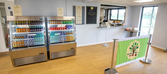 cropped image of the serving area at Cantley Park cafe showing a chiller filled with drinks, unattended serving hatch and a branded queue barrier