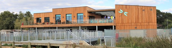 ultra-wide image of the Dinton Activity Centre, taken from some distance away, showing its timber-clad exterior and dragonfly badge on the upper wall