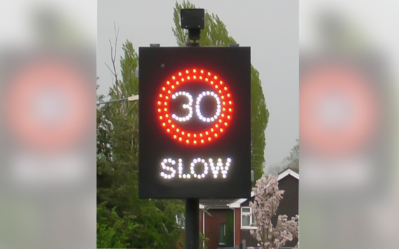 A vehicle activated speed sign with 30 in a red circle and slow down written underneath