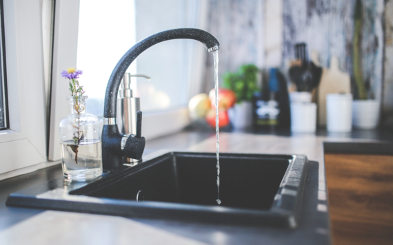 A running tap in a kitchen sink. Kitchen equipment slightly out of focus behind.