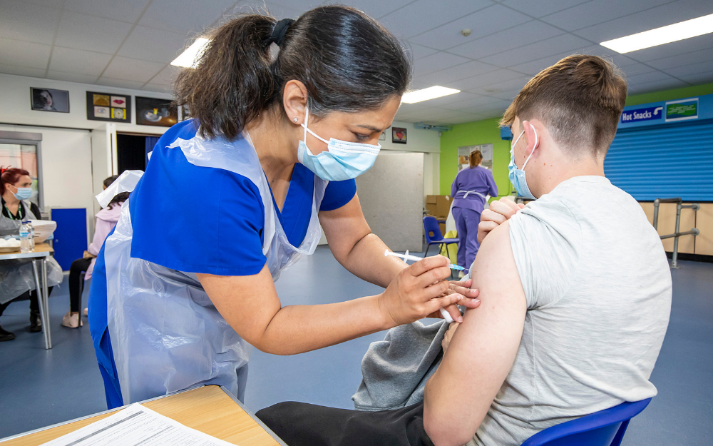 A Covid-19 vaccine is given to the left arm of a young man