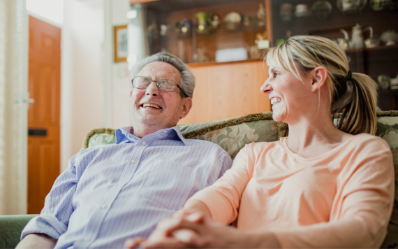 A man and a carer sat laughing together on a sofa 